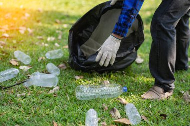 Adamın biri parkta temizlemek için plastik şişeleri siyah bir çöp torbasına koyuyor. Çevre dostu ve ekolojik açıdan Dünya Günü 'nde temizdir ve ücretsiz gelir karşılığında satılabilir..