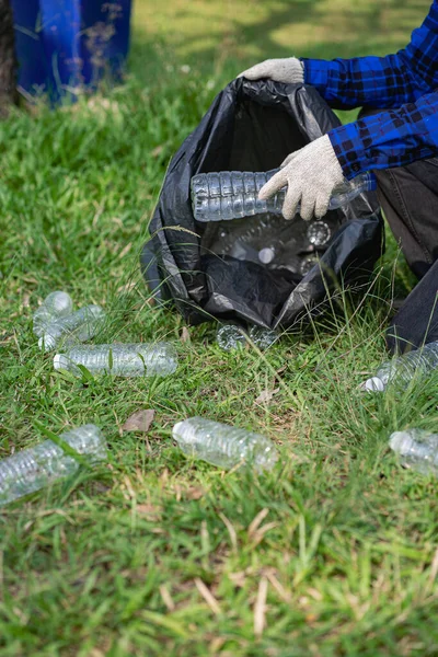 A man\'s hand puts plastic bottles in a black garbage bag to clean in the park. avoid pollution It is environmentally friendly and ecologically clean on Earth Day and can be sold for free income.