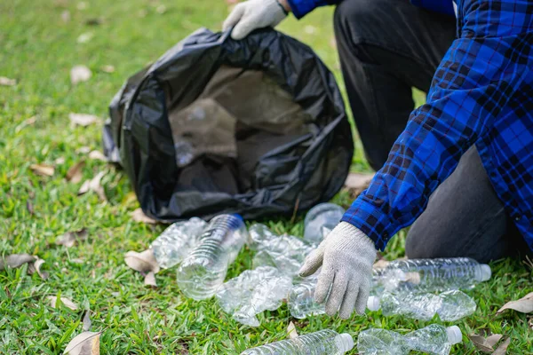 A man\'s hand puts plastic bottles in a black garbage bag to clean in the park. avoid pollution It is environmentally friendly and ecologically clean on Earth Day and can be sold for free income.