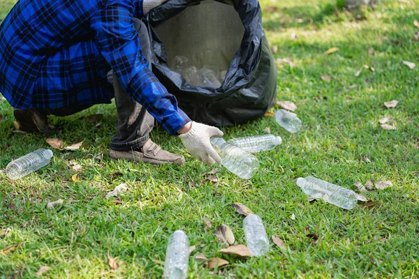 A man\'s hand puts plastic bottles in a black garbage bag to clean in the park. avoid pollution It is environmentally friendly and ecologically clean on Earth Day and can be sold for free income.