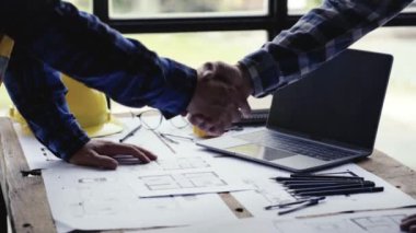 İki inşaat mühendisi ya da miğfer tutan miğfer ve el sıkışma ofis şantiyesinde yapılan büyük bir projeden sonra. Mühendis, bir inşaat projesi ekip çalışması ve işbirliği konsepti çiziyor. 4k