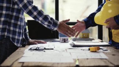 İki inşaat mühendisi ya da miğfer tutan miğfer ve el sıkışma ofis şantiyesinde yapılan büyük bir projeden sonra. Mühendis, bir inşaat projesi ekip çalışması ve işbirliği konsepti çiziyor. 4k