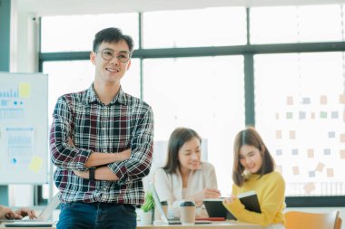 Genç bir adam arka planda çalışan bir bayan arkadaşıyla bir masanın önünde duruyor..