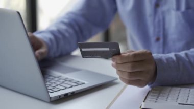 Adamın elinde kredi kartı var. Evdeki modern dizüstü bilgisayarla online ödeme yapıyor. Masa başında oturuyor, finans, internet üzerinden alışveriş yapıyor..
