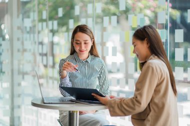 İki Asyalı iş kadını bir toplantıda fikirlerini tartıştı. İki kişi yatırım projeleri ve planlama stratejileri hakkında tartıştı. İşadamı ofiste dizüstü bilgisayarla konuşuyor.