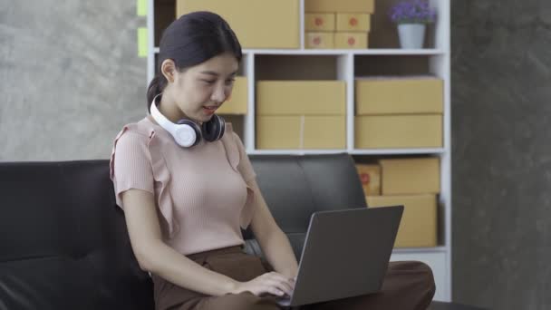 Asian Woman Wearing Headphones Her Neck Using Laptop Work Sofa — Stockvideo