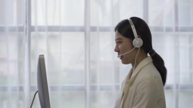 Çağrı merkezi Asyalı kadın, bir internet müşteri hizmetleri çalışanı, müşterilere telefonla yardım. Kulaklık takan ya da kulaklık takan resmi bir takım elbiseyle modern bir ofiste müşterilerle konuşuyor..