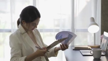 Finansal grafik belgeleriyle çalışan Asyalı kadın muhasebeci, çizelgeler için vergileri hesaplıyor ve ev gelirlerinin grafiklerini çıkarıyor. Dizüstü bilgisayarda çalışan ve harcama bütçesi planlayan iş kadını.