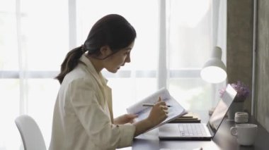 Finansal grafik belgeleriyle çalışan Asyalı kadın muhasebeci, çizelgeler için vergileri hesaplıyor ve ev gelirlerinin grafiklerini çıkarıyor. Dizüstü bilgisayarda çalışan ve harcama bütçesi planlayan iş kadını.