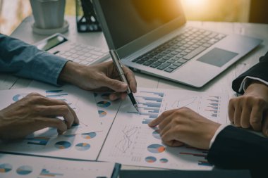 İki iş ortağı bütçe toplantıları sırasında mali ve şirket planlama grafiklerini tartışıyor ve iş adamı ofisteki dizüstü bilgisayarda yatırım pazarlama analizi planlıyor..