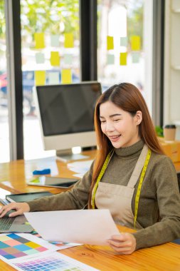 Bir atölyedeki Asyalı terziler, dizüstü bilgisayarı olan bir stüdyoda mezuraları, mankenleri ve kağıt taslakları olan şık genç tasarımcılarla çalışıyorlar. KOBİ iş konsepti İnternet üzerinden kıyafet sat.