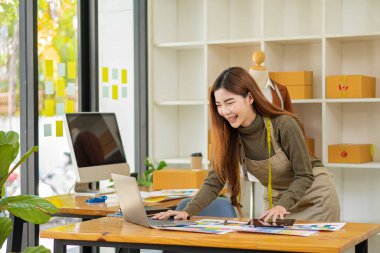 Bir atölyedeki Asyalı terziler, dizüstü bilgisayarı olan bir stüdyoda mezuraları, mankenleri ve kağıt taslakları olan şık genç tasarımcılarla çalışıyorlar. KOBİ iş konsepti İnternet üzerinden kıyafet sat.