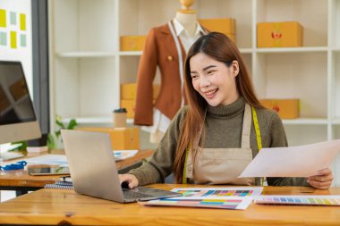 Bir atölyedeki Asyalı terziler, dizüstü bilgisayarı olan bir stüdyoda mezuraları, mankenleri ve kağıt taslakları olan şık genç tasarımcılarla çalışıyorlar. KOBİ iş konsepti İnternet üzerinden kıyafet sat.
