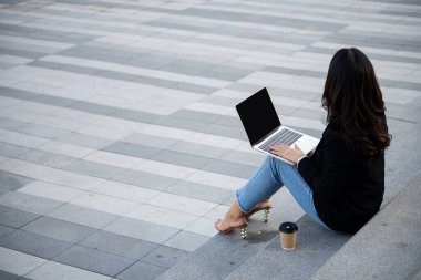 Diz üstü bilgisayarı olan Asyalı bir iş kadını iş bölgesindeki ekranlara bakıyor, profesyonel kadınlar dışarıda oturuyor.