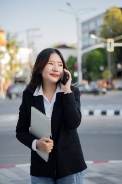 Dışarıda akıllı bir telefonla çalışan Asyalı bir iş kadını iş bölgesindeki bir ekrana bakıyor. Profesyonel kadın dışarıda oturuyor.