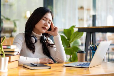 Asyalı üniversite öğrencisinin dizüstü bilgisayarla çalıştığı için başı ağrıyor..