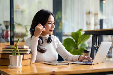Güzel Asyalı kız üniversite öğrencisi dizüstü bilgisayarda çalışıyor. İnternet 'te konseptlerle ilgili bilgi aramak, çalışmak, bir kafede çalışmak..