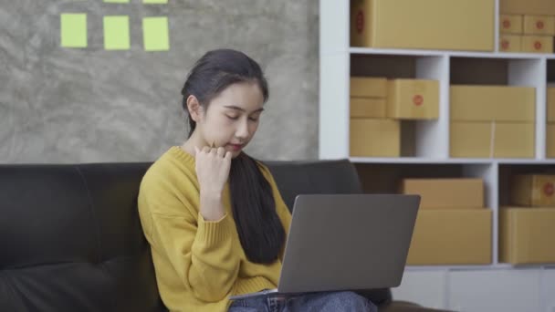 アジアの女性を保持クレジットカードオンラインショッピング上のラップトップ上の自宅でソファ — ストック動画