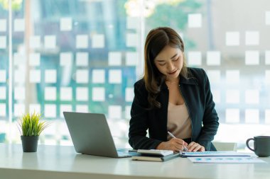 Modern ofiste dizüstü bilgisayar kullanan Asyalı iş kadını finansal grafikler ve emlak yatırım verileriyle bir hesap analizi raporu hazırlıyor. finansal ve vergi sistemi kavramları