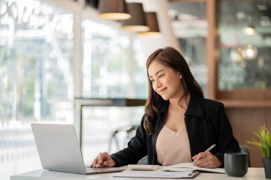 Modern ofiste dizüstü bilgisayar kullanan Asyalı iş kadını finansal grafikler ve emlak yatırım verileriyle bir hesap analizi raporu hazırlıyor. finansal ve vergi sistemi kavramları