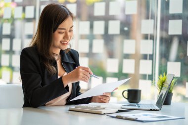 Modern ofiste dizüstü bilgisayar kullanan Asyalı iş kadını finansal grafikler ve emlak yatırım verileriyle bir hesap analizi raporu hazırlıyor. finansal ve vergi sistemi kavramları