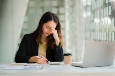 Asyalı bir iş kadını, ofiste uzun saatler boyunca dizüstü bilgisayara baktığı için göz yorgunluğundan muzdarip..