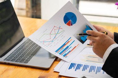 Finansal veri ellerindeki kalemle çalışan iş adamları, masa vergisi konseptinde dizüstü bilgisayar kullanarak yıllık iş raporu analiz raporlarına işaret ediyorlar.