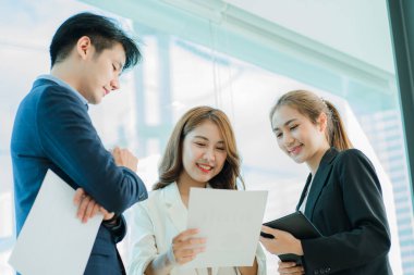 Üst düzey bir ofisteki çok ırklı genç bir iş ekibi dizüstü bilgisayarda oturup mutlu bir gülümsemeyle evrak işleriyle uğraşıyor. Asyalı iş adamları grubu modern ofis tasarım ve konsept planlamada toplanıyor.
