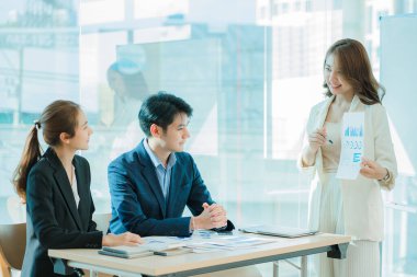 Üst düzey bir ofisteki çok ırklı genç bir iş ekibi dizüstü bilgisayarda oturup mutlu bir gülümsemeyle evrak işleriyle uğraşıyor. Asyalı iş adamları grubu modern ofis tasarım ve konsept planlamada toplanıyor.