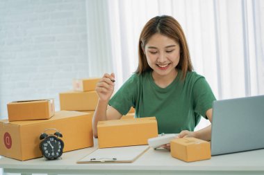 Independent SME Small Business Entrepreneur Portrait of an Asian woman working at home with a laptop taking orders and Online Marketing Packaging Shipping Boxes eCommerce business idea