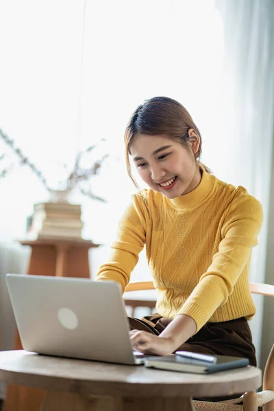 Happy smiling Asian woman relaxing using laptop computer in bedroom at home. creative young girl working and typing on keyboard Study and work from home concept, vertical image.