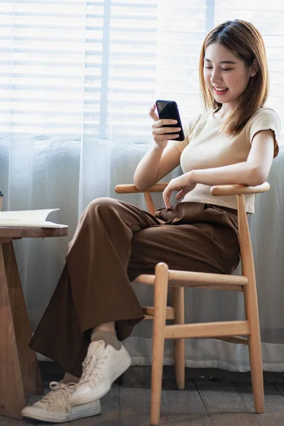 Happy smiling Asian woman relaxing using a smartphone to talk and laptop computer in the bedroom at home. creative girl working and typing on keyboard Study and work from home vertical image concept