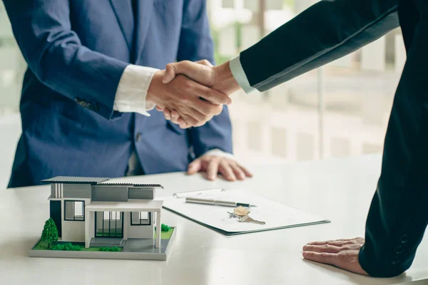 Sales agents and landlords when signing a contract to buy or rent a new home. Real estate agents shake hands with customers after signing contracts. Contract documents and house plans on a wooden table
