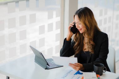 Freelance Asian woman working on smartphones and tablet computers in a modern office. make an account analysis report on real estate investment information financial and tax system concepts