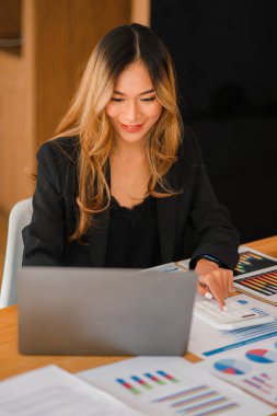 Modern ofiste dizüstü bilgisayarla çalışan Asyalı genç bir iş kadını. gayrımenkul yatırım bilgileri, muhasebe kavramları, finansal sistemler ve vergiler.