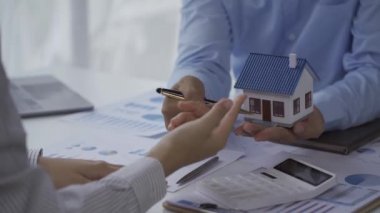 Emlakçılar ve müşteriler sözleşmeleri tartışıyorlar. Ev Mortgage Gayrimenkul Fikirleri İçin Faiz Oranları Satıcısı Mini Ev Modelini Yeni Aile 4k Videosuna Gösteriyor