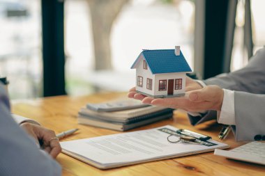 Bir emlakçı ya da banka memuru, ev satış sözleşmesi ya da ofis kredisi olan müşterilere verilen kredinin faizini açıklar. Satıcı model evler satın alan müşteriler için sigorta tavsiye eder.