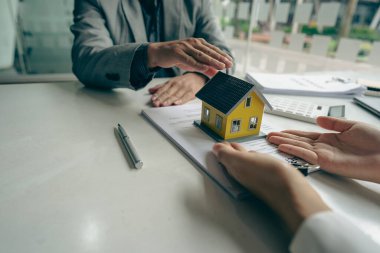 Bir emlakçı ya da banka memuru, ev satış sözleşmesi ya da ofis kredisi olan müşterilere verilen kredinin faizini açıklar. Satıcı model evler satın alan müşteriler için sigorta tavsiye eder.
