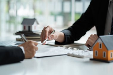 Bir emlakçı ya da banka memuru, ev satış sözleşmesi ya da ofis kredisi olan müşterilere verilen kredinin faizini açıklar. Satıcı model evler satın alan müşteriler için sigorta tavsiye eder.