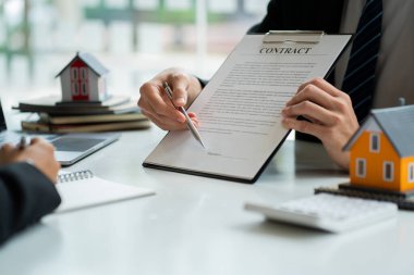 Bir emlakçı ya da banka memuru, ev satış sözleşmesi ya da ofis kredisi olan müşterilere verilen kredinin faizini açıklar. Satıcı model evler satın alan müşteriler için sigorta tavsiye eder.