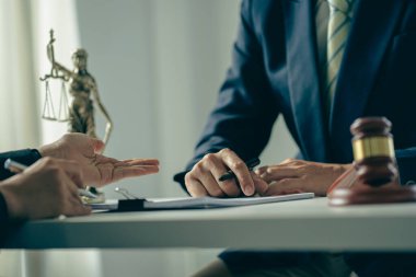 Erkek işadamı ve avukat, hukuk alanında müvekkil ekibine danışmanlık yapıyor, yasal hizmetler masasında hakimin ölçeği ve çekiciyle ofis sözleşmesini tartışıyor ve imzalıyor..