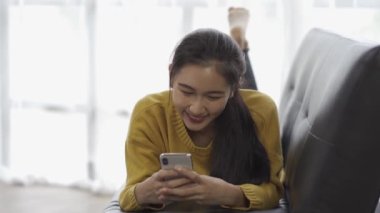 Asyalı kadın telefonda oynamaktan ve evdeki kanepede arkadaşlarıyla konuşmaktan hoşlanıyor..