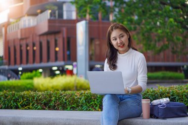 Beautiful schoolgirl learning with laptop computer while sitting on the floor outdoors, online learning concept.