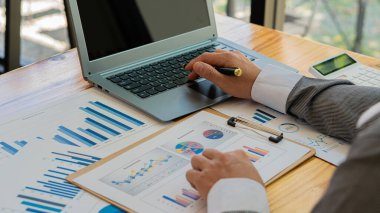 A business accountant or financial professional analyzes business report graphs with a laptop and charts at the company office. and stock market research, concepts, economics, finance