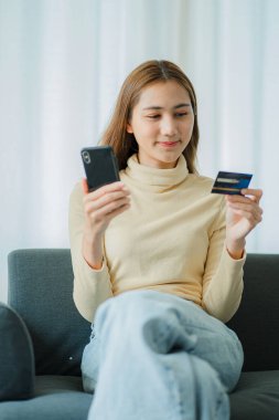 Kanepe üzerinde dinlenen çekici Asyalı kadınlar kredi kartı sahipleri ve akıllı telefonlar internetten alışveriş yapabilirler. Evde online bankacı kız cep telefonu alışverişi yapıyor.