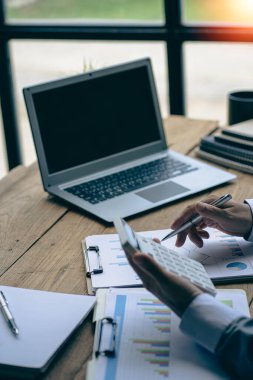 Businessman hand holding a pen to work with charts, graphs and analyze business strategies. financial statistics with laptop sit at desk vertical view