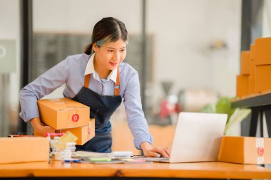 Asyalı, bağımsız, KOBİ işi, online alışveriş bir dizüstü bilgisayarda paket kutusu ile çalışıyor. Çevrimiçi bir KOBİ şirketinin kavramı ve teslimi