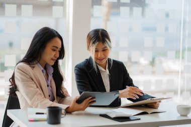 Masada dizüstü bilgisayarları ve finansal belgeleri olan iki Asyalı kadın muhasebeci var..