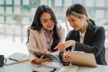 Masada dizüstü bilgisayarları ve finansal belgeleri olan iki Asyalı kadın muhasebeci var..