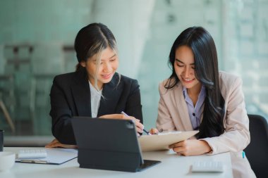 Masada dizüstü bilgisayarları ve finansal belgeleri olan iki Asyalı kadın muhasebeci var..